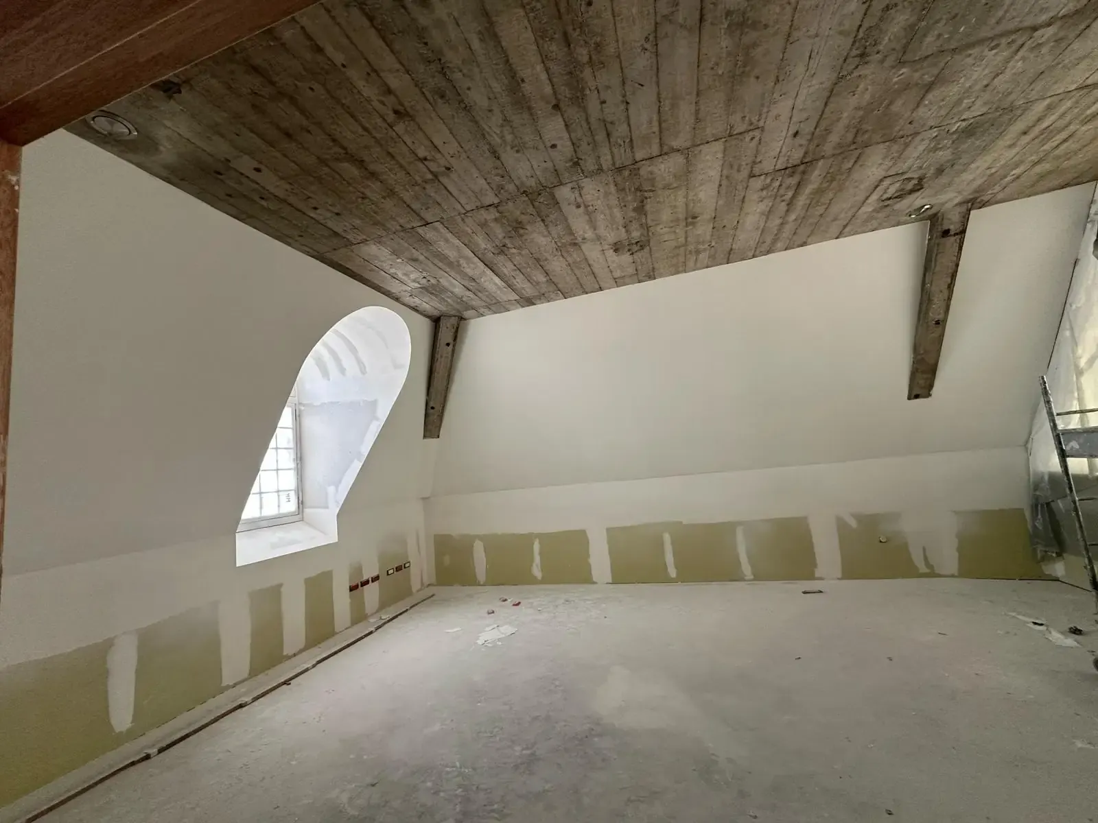 Combles du Palais du Tau à Reims pendant le chantier : dalle de béton coffrée en planches au-dessus, lucarne cintrée au fond.