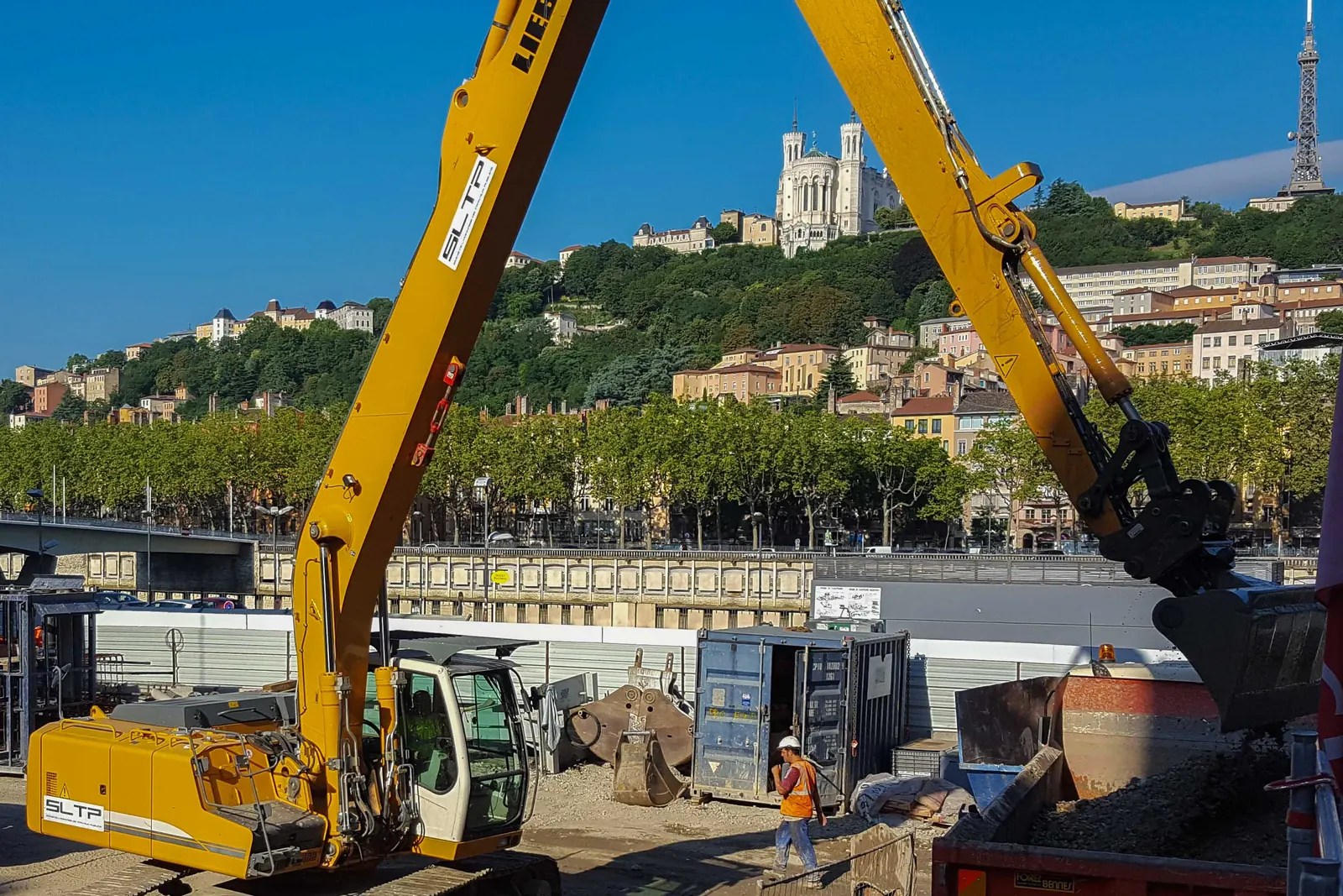 Pelle Liebherr jaune siglée SLTP sur le chantier du parking Saint-Antoine, à Lyon ; en fond, la colline et la basilique de Fourvière.