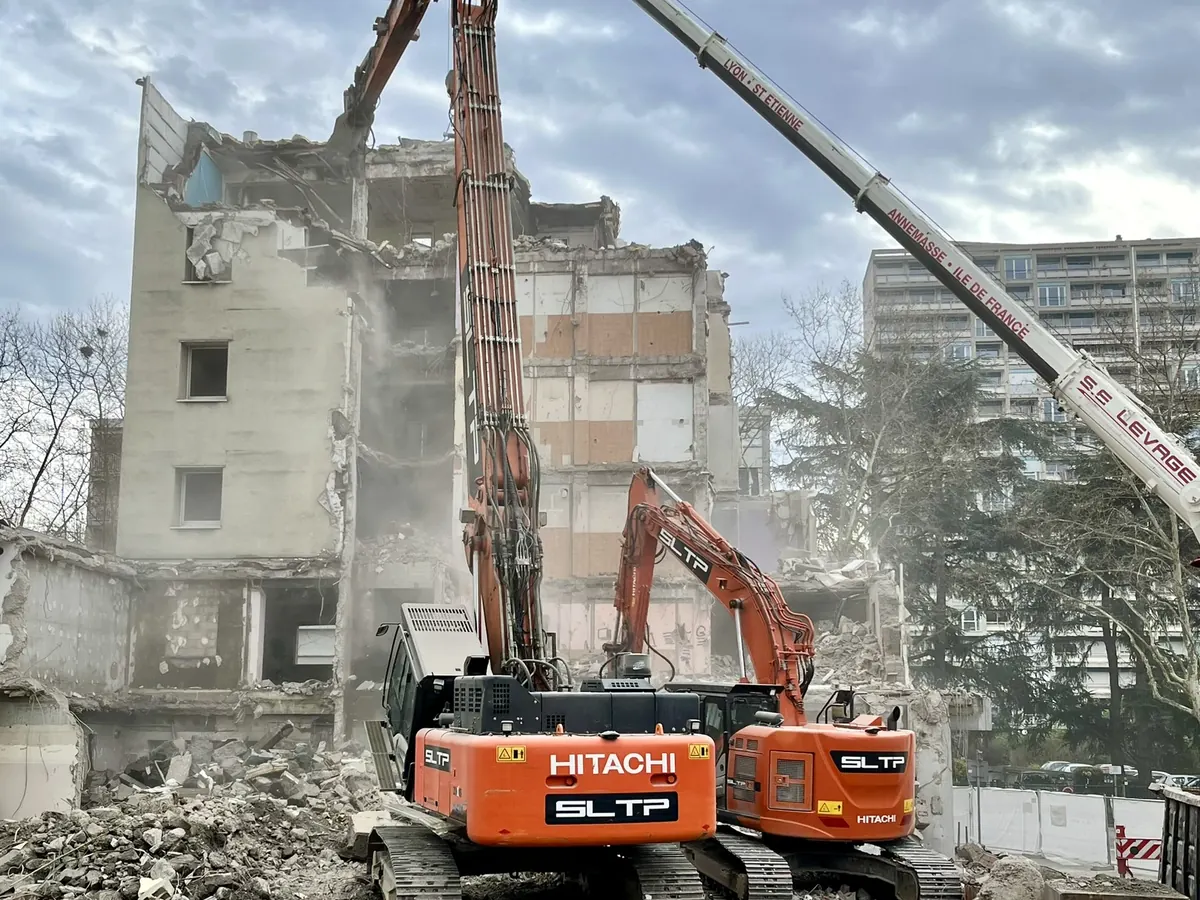 Deux pelles Hitachi orange siglées SLTP, dont une à grand bras, devant l’immeuble en démolition de la Clinique Tonkin, à Villeurbanne.